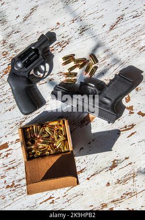 Una pistola semiautomatica 9mm Glck, una revolver Ruger da 9 mm, conchiglie e una scatola di cartucce in una scatola di cartone su un tavolo di legno. Foto Stock