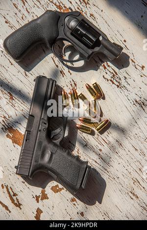 Un nero, Glock 19, 9mm, pistola e un Ruger, 9mm, snub naso, revolver su un tavolo di legno insieme con alcuni proiettili. Foto Stock
