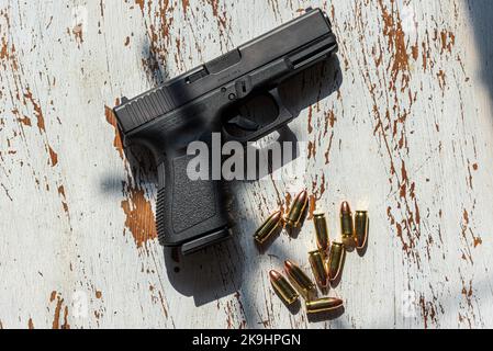 Una pistola semi-automatica da 9mm Glock 19, realizzata in Austria, appoggiata su un tavolo di legno, insieme ad un gruppo di 9mm proiettili. Foto Stock