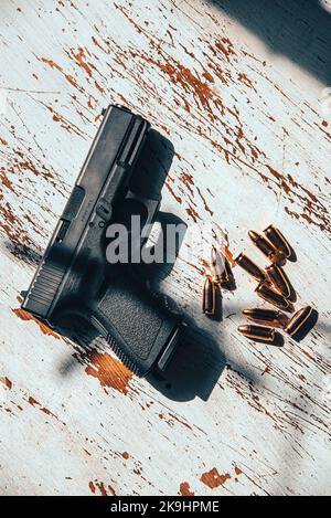 Una pistola semi-automatica da 9mm Glock 19, realizzata in Austria, appoggiata su un tavolo di legno, insieme ad un gruppo di 9mm proiettili. Foto Stock