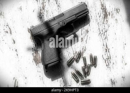 Una pistola semi-automatica da 9mm Glock 19, realizzata in Austria, appoggiata su un tavolo di legno, insieme ad un gruppo di 9mm proiettili. Foto Stock