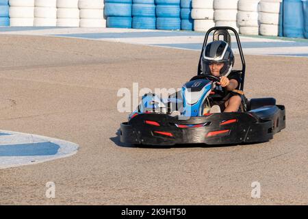 un ragazzo adolescente alla guida di un kart all'uscita di una curva di un circuito karting, faccia di velocità e concentrazione mentre guida un go kart Foto Stock