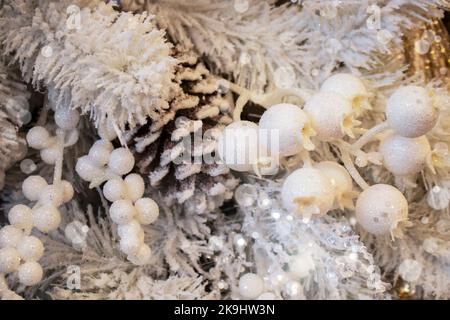 Sfondo natalizio di bacche bianche scintillanti e coni di pino innevati con fiocco di bokeh e lente - bianco e oro Foto Stock