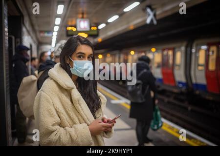 La giovane ragazza indiana a Londra attende il suo tubo mentre la messaggistica sul telefono cellulare. Foto Stock