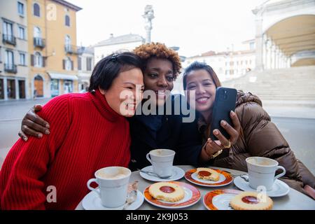 Tre amiche che guardano qualcosa sul cellulare durante la colazione. Foto Stock