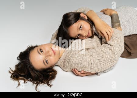 bruna mamma e figlia in intimo maglieria sorridendo alla macchina fotografica e abbracciando su sfondo grigio Foto Stock