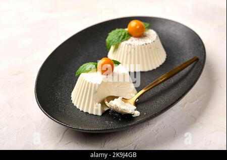 Cucchiaio e mangiato panna cotta fatta in casa con baccello di vaniglia naturale, physalis o ciliegia invernale e menta, fuoco selettivo Foto Stock