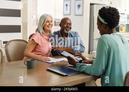 Felice coppia anziana diversa che parla con la consulente finanziario femminile afro-americana Foto Stock