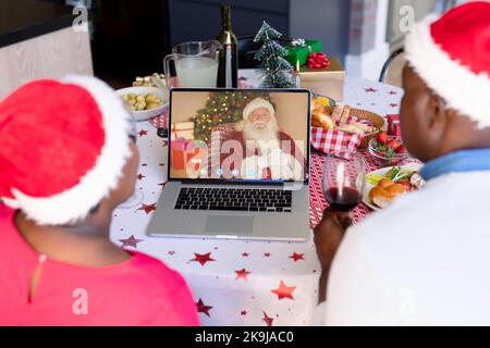 Coppia afroamericana anziana con videochiamata con l'uomo caucasico che indossa il costume di babbo natale Foto Stock