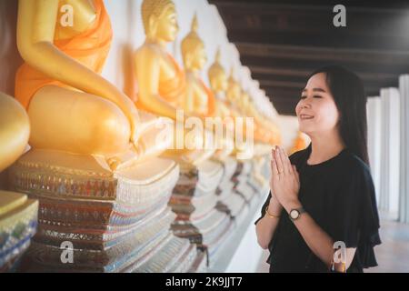 Bella donna asiatica rende omaggio alla statua del Buddha con rispetto e fede Foto Stock