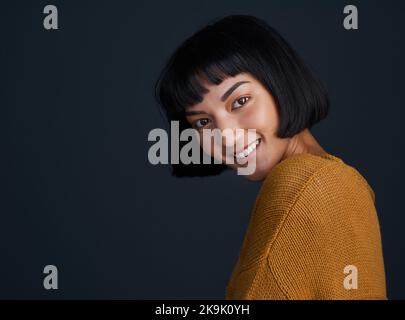 Un incantatore di nota. Studio shot di una giovane donna attraente che posa su uno sfondo scuro. Foto Stock