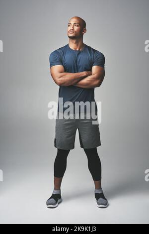 Entrare nella zona fitness. Studio shot di un giovane atletico in piedi con le braccia incrociate su uno sfondo grigio. Foto Stock