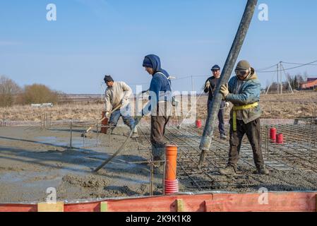 REGIONE DI LENINGRADO, RUSSIA - 28 MARZO 2021: I lavoratori ospiti versano la fondazione di una casa di campagna in un giorno di primavera Foto Stock