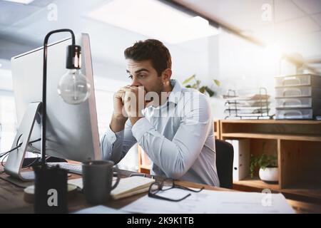 Lascia sperare che questo funzioni... un giovane uomo d'affari che guarda stressato mentre lavora tardi su un computer in un ufficio. Foto Stock