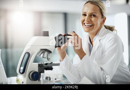 Si tratta di una soluzione innovativa. Ritratto ritagliato di un attraente scienziato maturo femmina utilizzando un microscopio mentre fare ricerche nel suo laboratorio. Foto Stock