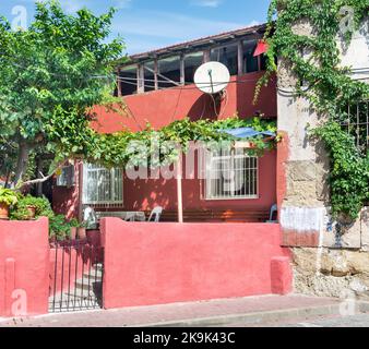 Facciata esterna di vecchia casa tradizionale dipinta di rosso, con finestre in ferro battuto, piante scalatrici, alberi verdi, quartiere Balat, Istanbul, Turchia Foto Stock