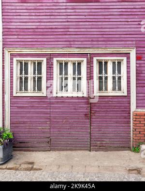 Grunge in legno intatto porte abbandonate dipinte in viola, con tre finestre in legno bianco dipinte in bianco, in un vicolo di ciottoli Foto Stock