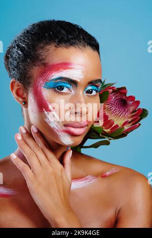 Dipinto come un protea. Studio ritratto di una bella giovane donna coperta di pittura sul viso che posa su uno sfondo blu. Foto Stock