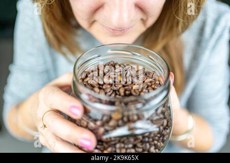 Donna che tiene in mano un vaso di vetro mentre odora l'aroma del caffè. Foto Stock