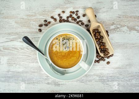 Tazza in porcellana bianca con caffè espresso appena preparato e chicchi di caffè sul tavolo. Foto Stock