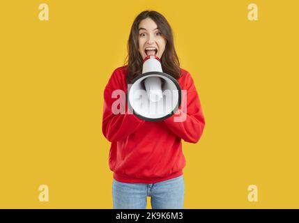 La giovane donna bruna che indossa una felpa rossa ride parlando in altoparlante su sfondo giallo. Foto Stock
