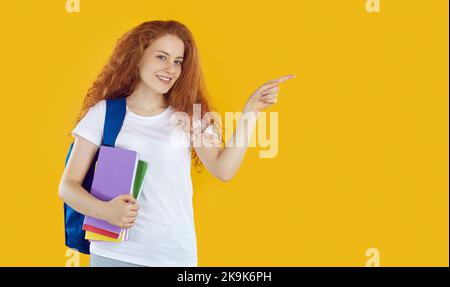 Bella studentessa che poiting con il suo indice dito a destra, isolato su sfondo arancione Foto Stock