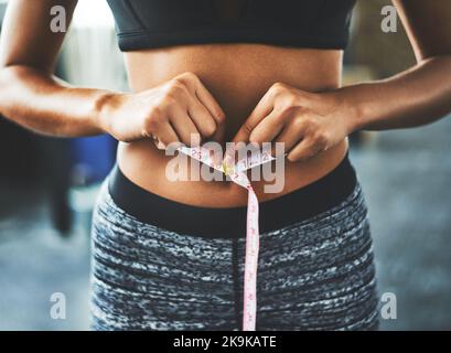 Quando la vostra routine di allenamento inizia a mostrare i risultati. Una giovane donna in forma che misura la vita in palestra. Foto Stock