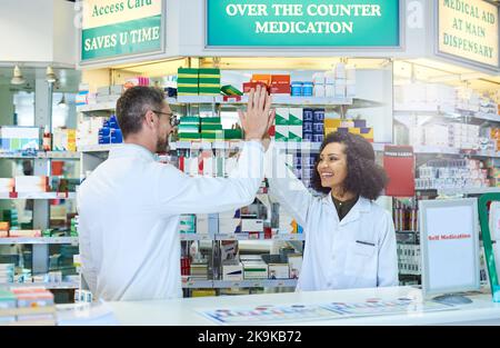 Motivati a fornire il meglio in assistenza medica. Un uomo maturo e una giovane donna che si donano un alto cinque mentre lavorano in farmacia. Foto Stock