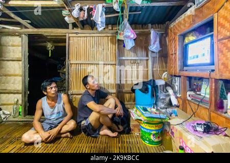 Due uomini filippini che guardano la TV nella loro casa natale a Batangas, nelle Filippine Foto Stock