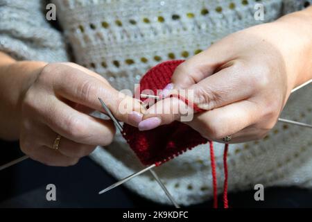 Donna mani calzino da maglieria con aghi e filo di colore rosso. Primo piano delle mani Foto Stock