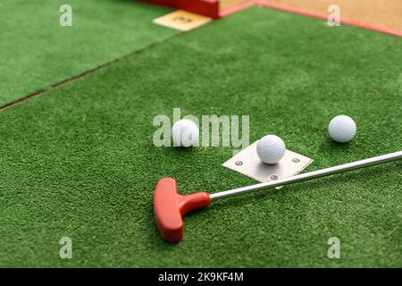 Putters e palle da golf in miniatura assortiti si inclinano su erba sintetica. Foto Stock