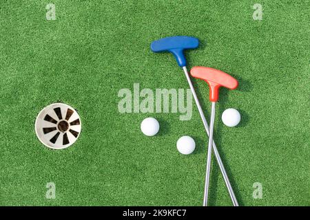 Putters e palle da golf in miniatura assortiti si inclinano su erba sintetica. Foto Stock