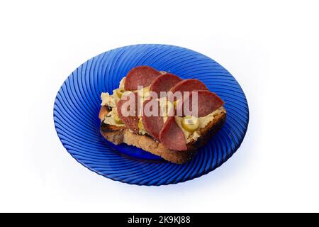 Fetta di pane tostato con hummus di ceci e fette di salame fritte, su un piatto di vetro blu Foto Stock