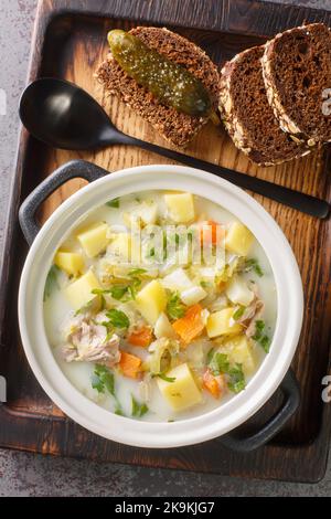 Zuppa di aneto zupa ogorkowa è una delle zuppe tradizionali più popolari in Polonia primo piano sul piatto sul vassoio di legno. Vista dall'alto verticale da ab Foto Stock