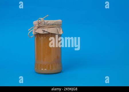 Marmellata di mele in un vaso di vetro coperto di carta, su sfondo blu. Foto Stock