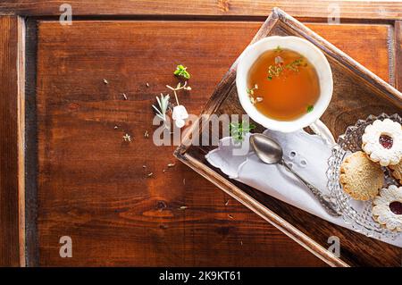 Tazza da tè con foglie di erbe fresche e biscotti su sfondo di legno, vista dall'alto, posto per il testo. Concetto sano Foto Stock