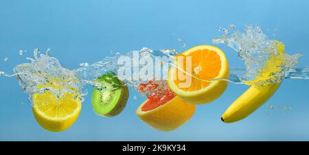 La frutta mescolata spruzzi in acqua pulita su fondo blu Foto Stock