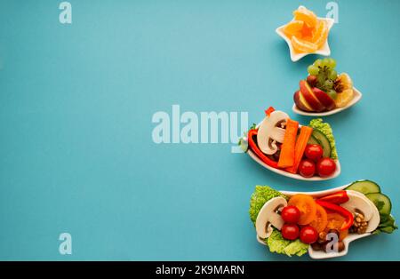 Piatto in forma di albero di Natale con verdure, frutta, funghi e bacche. Sfondo blu. Il concetto di prelibatezze vegetariane per gli holida Foto Stock