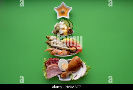 Piatto in forma di albero di Natale con cibo proteico - carne, pesce, formaggi, noci, ecc sfondo verde. Il concetto di keto dieta tratta per l'ho Foto Stock