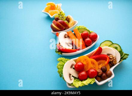 Primo piano piatto in forma di albero di Natale con verdure, frutta, funghi e bacche. Sfondo blu. Il concetto di delizie vegetariane per la t Foto Stock