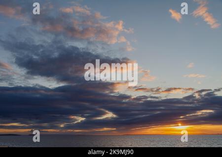 Il sole che tramonta illumina l'orizzonte lungo la costa gallese Foto Stock