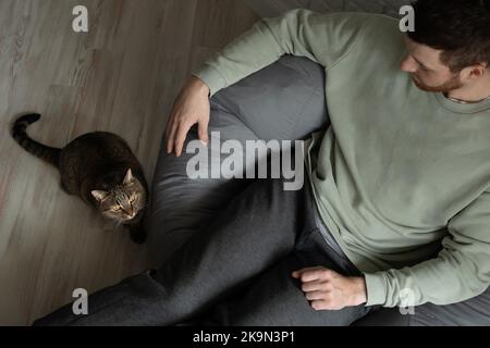 il proprietario è seduto su una sedia per borse e il suo gatto è seduto accanto a lui. Foto Stock
