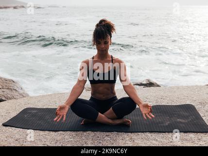 Donna in loto posa seduta su materassino yoga in riva al mare al tramonto Foto Stock