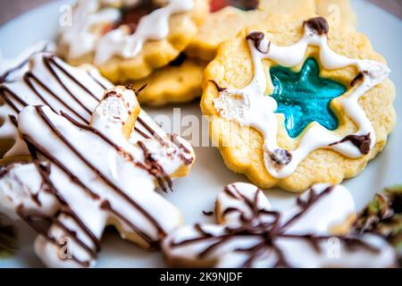 Macro primo piano di piatto bianco riempito con biscotti di Natale smaltati decorati in casa con zucchero candito glassa e gelatina colorata blu cotta in vacanza Foto Stock