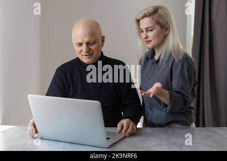 Vista frontale Happy anziani 70s uomo grigio pelato imparare utilizzando il software del computer con cura figlia cresciuta, anziani pensionati e tecnologia moderna Foto Stock