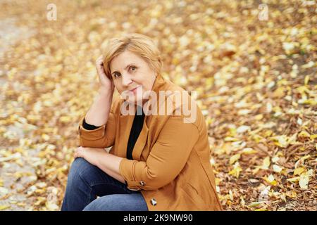 Stagione di caduta o pensione: Primo piano ritratto di attraente donna caucasica anziana a piedi nel parco autunnale. Gente anziana sorridente e matura che gode la natura. Foto di alta qualità Foto Stock
