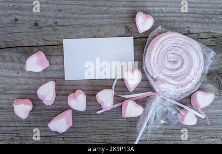Carta e marshmallow rosa giacciono su una tavola di legno Foto Stock