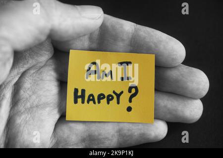 Un uomo che tiene un pezzo di carta giallo con la domanda sono felice di aver scritto su di esso nel palmo della sua mano. Primo piano. Foto Stock