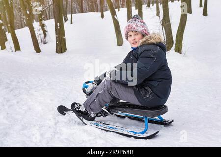 In inverno, un ragazzo guida uno scooter da neve all'aperto. Vacanze e vacanze invernali Foto Stock