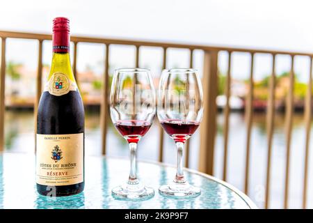 Hollywood, USA - 12 luglio 2021: Bicchieri Wineglass in bottiglia di vino rosso francese versato Cotes Du Rhone Famille Perrin sul balcone di vetro a Miami, Florida Foto Stock